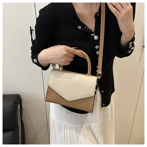 Detail of a beige woven texture and brown leather handbag with gold metal hardware