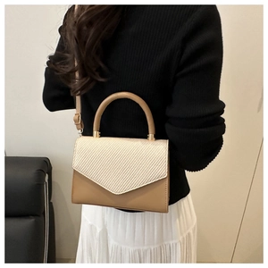Détail d'un sac enveloppe en cuir kaki avec rabat tissé beige et boucles métalliques dorées