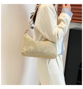 Detail view of a beige straw tote bag with knot strap on a model wearing white