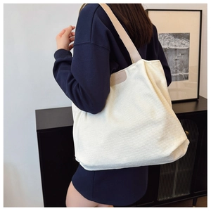 Detail of white corduroy tote bag featuring leather handles and 'FASHION' patch