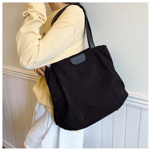 Detail of black corduroy tote bag featuring a leather Fashion patch and long shoulder straps