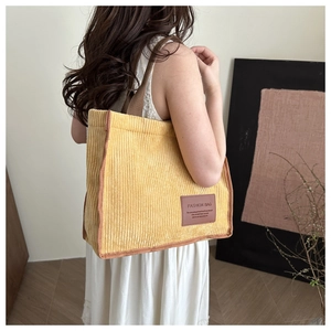 Detail of yellow corduroy tote bag with vertical texture and brown leather logo patch