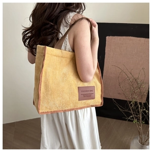 Detail of yellow corduroy tote bag featuring dark brown trim and branded leather patch