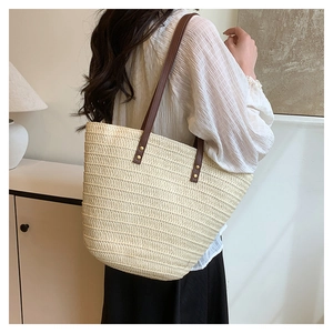 Detail of woven straw tote bag with brown leather handles and metal rivet fasteners