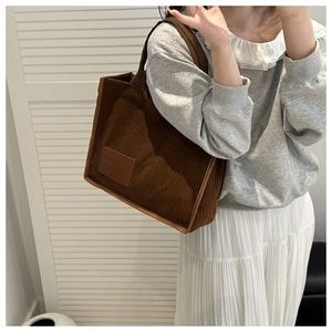 Detailed view of coffee corduroy tote bag with leather tag on model with pleated skirt