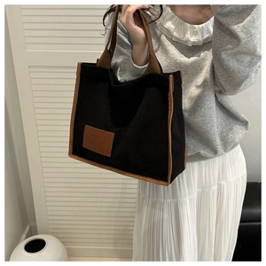 Detail of black corduroy tote bag with brown leather trim held by a female model