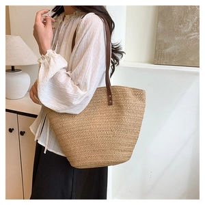 Vue latérale du sac fourre-tout en paille avec bandoulières en cuir marron en intérieur