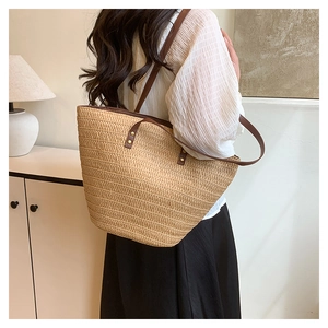 Detail of woven straw tote bag with brown leather strap and metal rivet reinforcement