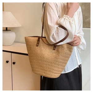 Detailed close-up of woven straw tote bag with brown leather handles and metal rivets