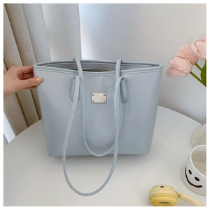 Détail du sac cabas bleu clair avec plaque en métal argenté sur un bureau blanc