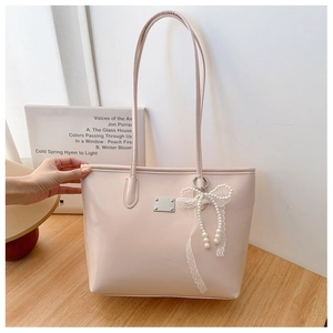 Détail d'un cabas beige clair avec pendentif perle et nœud en dentelle sur bois