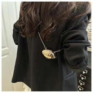 Detail of metallic gold shell bag with liquid metal texture on black suit