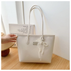 Vue détaillée du sac cabas blanc crème avec plaque argentée et breloque nœud perlé