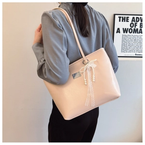 Détail du sac cabas rose clair avec texture cuir, nœud en dentelle et breloque perle