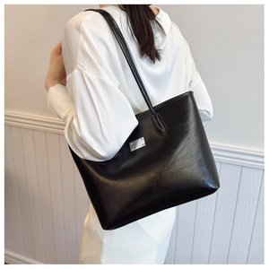 Sac fourre-tout noir minimaliste avec plaque en argent porté par un mannequin en tenue chic