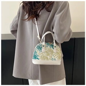 Detail of white seashell crossbody bag with tropical leaf embroidery and gold hardware