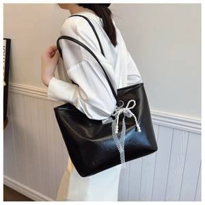 Détail du grand sac cabas noir brillant avec pendentif nœud en perles porté à l'épaule