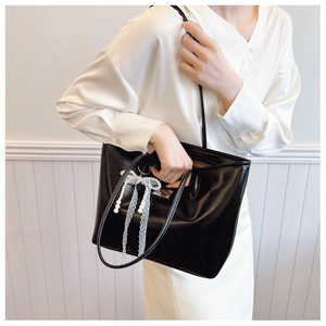 Détail d'un sac cabas en similicuir noir avec nœud en dentelle et breloque en perles