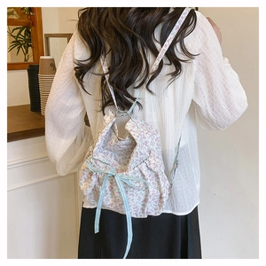 Close-up of floral drawstring backpack with blue checkered bow on model in a cafe