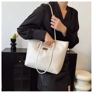 Sac cabas chic en cuir crème porté par un mannequin avec poignée minimaliste et plaque en métal