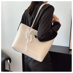 Détail du sac cabas crème avec charm perle et nœud en dentelle porté à l'épaule