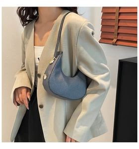 Nahaufnahme einer blauen halbmondförmigen Hobo-Tasche mit goldener Schnalle an der Schulter