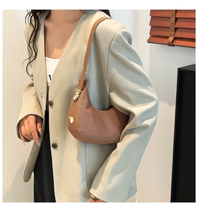 Braune Halbmond-Schultertasche mit Gold-Hardware, getragen von einem Modell im Anzug