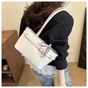 Model wearing a white patent leather tote bag with a pink plaid ribbon accent