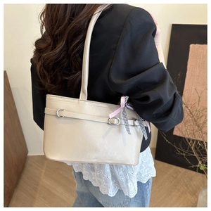 Dettaglio della borsa a spalla in pelle verniciata beige con fiocco su una modella