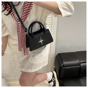 Detail of black woven shoulder bag with silver star emblem on a leather sofa
