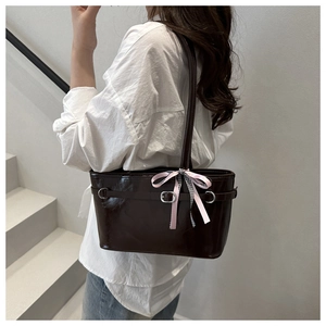 Dettaglio di una borsa a spalla marrone lucida con un fiocco decorativo rosa e a quadri