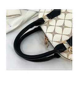 Detail of white monogrammed shell bag with black handles and golden zipper hardware