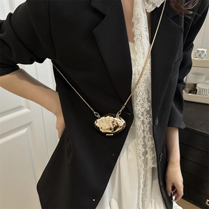 Chic mini gold oval chain bag with wavy mirror finish worn on a black blazer suit