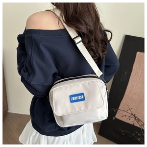 Detail of a cream nylon crossbody bag with adjustable strap worn by a model in lifestyle setting
