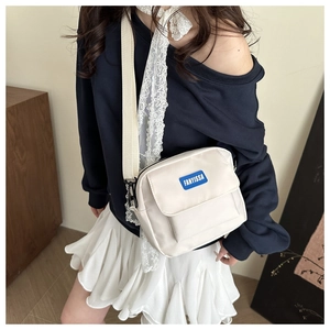 Detail of cream nylon crossbody bag with blue rubber logo patch and wide shoulder strap