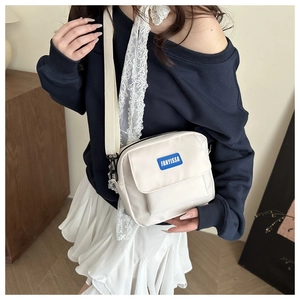 Detail of cream white nylon crossbody bag featuring blue FANYISSA label and canvas strap