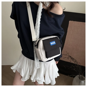 Detail of a black and white canvas crossbody bag with a blue FANYISSA label on a model