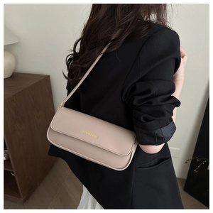 Detail view of the beige baguette bag with gold lettering shown on a model shoulder