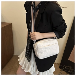 Detailed close-up of woven white leather camera bag with wide colorful striped strap