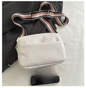 Size comparison of white woven crossbody bag with striped strap and smartphone detail