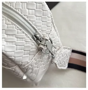 Detail of silver zipper closure and woven texture on a white crossbody phone bag