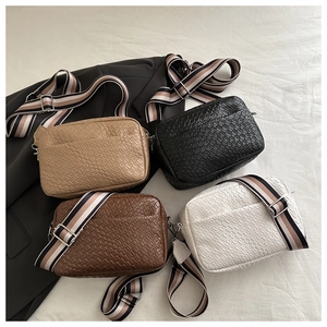 Flat lay of four woven texture crossbody camera bags with striped wide shoulder straps