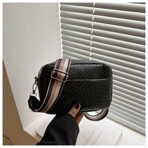 Close-up of woven black leather texture on a crossbody bag with a striped fabric strap
