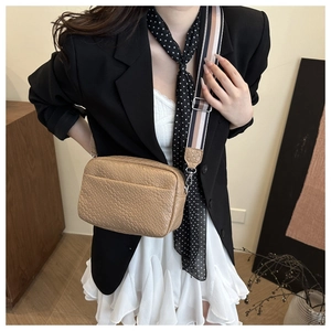 Detail of light brown crocodile pattern crossbody bag with a colorful striped wide strap