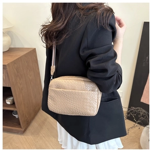 Detail of beige woven texture crossbody bag with striped shoulder strap on model