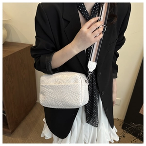 Detail of white woven texture crossbody bag with wide striped fabric shoulder strap