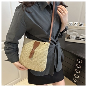 Detalle del bolso tipo cubo de paja tejida con correa de cuero marrón y hebilla