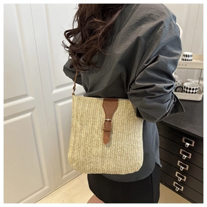 Detailed view of beige woven straw shoulder bag with brown leather strap and gold buckle