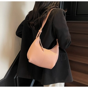 Detail of a dusty pink leather crescent shoulder bag worn with a black blazer for work