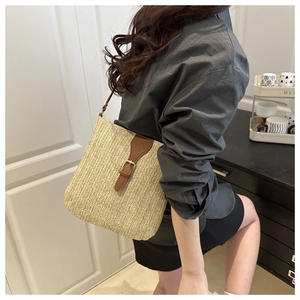 Detail view of woven straw shoulder bag with brown leather strap and metal buckle closure